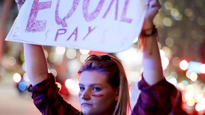 Mulher segura cartaz exigindo salários iguais