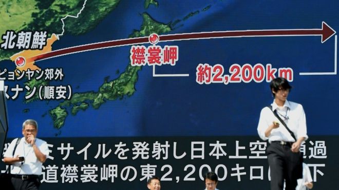 Ciudadanos caminan frente a una gran pantalla en Japón que muestra la trayectoria del último misil norcoreano.