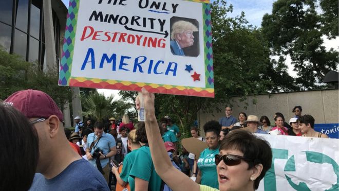 A demonstrator in Texas holds aloft a sign with a caricature of Donald Trump and the words: The only minority destroying America