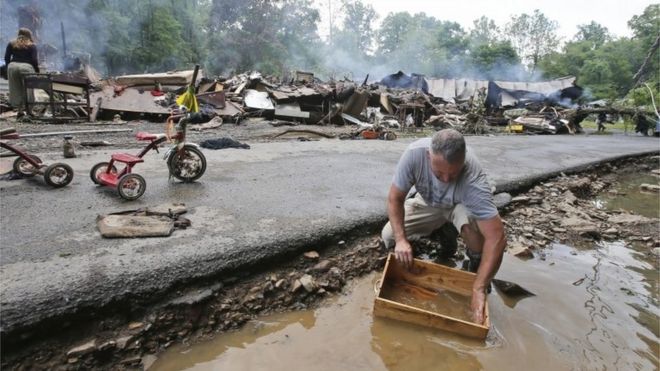 A man cleans out a box with creek water as he cleans up from severe flooding in White Sulphur Springs, West Virginia.