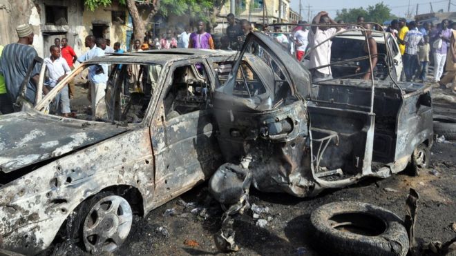 People gather to look at a burnt vehicles at the site of a bomb explosion that rocked the busiest roundabout near the crowded Monday Market in Maiduguri, Borno State, on July 1, 2014.