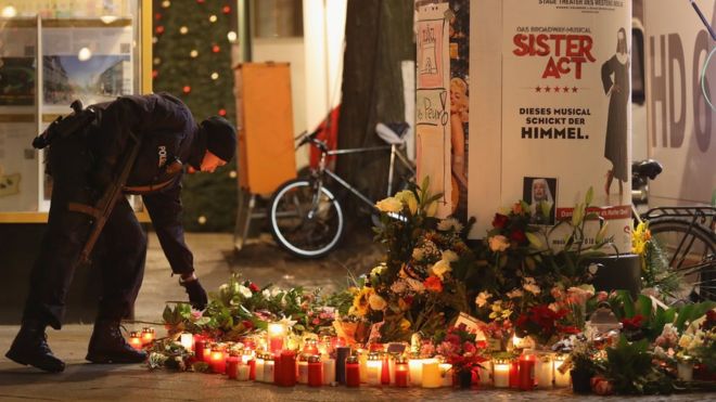 A policeman places a candle on behalf of a mourner at a makeshift memorial the day after a truck drove into a crowded Christmas market in the city center on December 20, 2016 in Berlin, Germany.