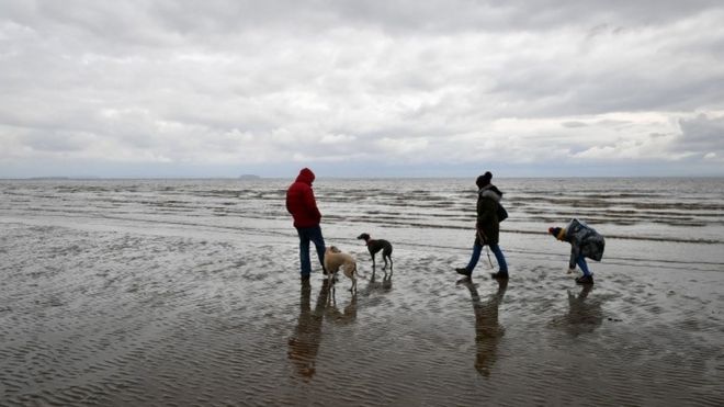 People walk their dogs on Barry Island beach, Wales