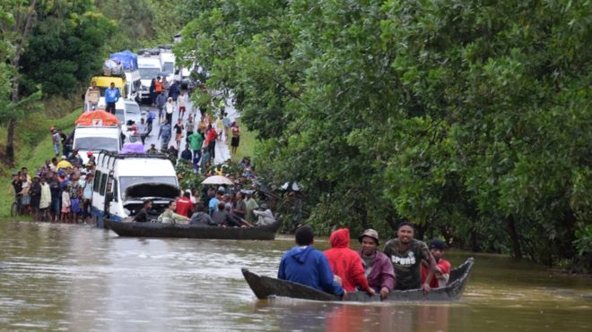Two boats carrying men float on a lake in Madagascar as several vans and people look on. The chaos was cause by tropical storm Eliakim near Manambonitra, Atsinanana region, Madagascar.
