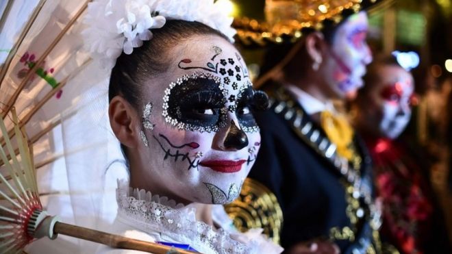 A woman wearing elaborate make-up and holding an umbrella takes part in the parade.