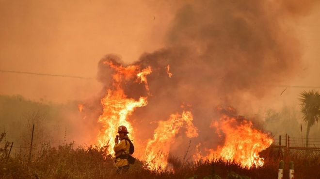 Flames leap along the 101 freeway in La Conchita, Ventura County, as a firefighter stands nearby on December 7, 2017