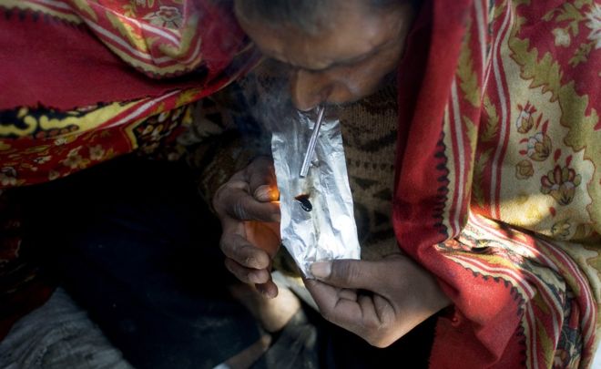 Idian drug user covers himself with a blanket as he smokes smack, heroin, in old Delhi