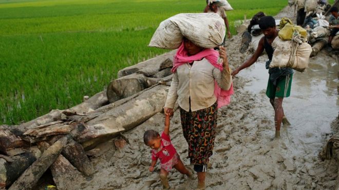 A Rohingya refugee woman holds her child as they walk on the muddy path after crossing the Bangladesh-Myanmar border in Teknaf, Bangladesh, 3 September 2017