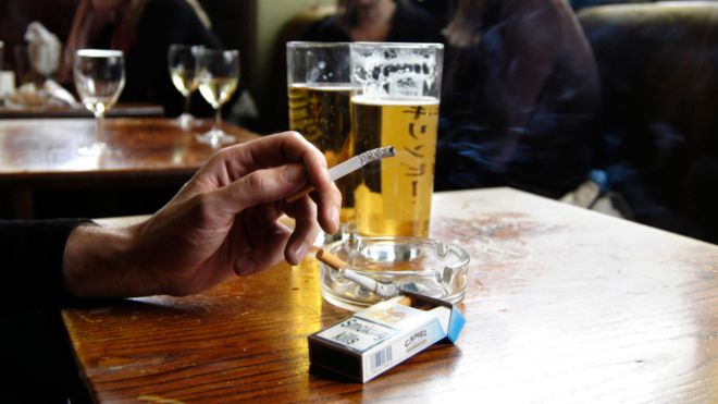 Hand holding a half-smoked cigarette at a pub table, beer glasses in the background