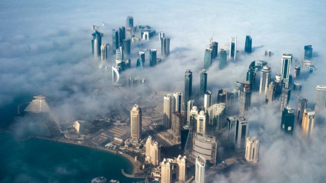 An aerial view of high-rise buildings emerging through fog covering the skyline of Doha