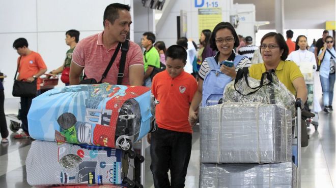 Passengers push carts with their baggage wrapped in plastic and cloth