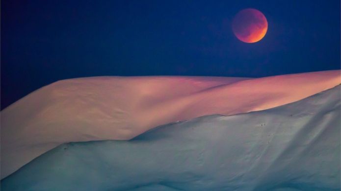 A super blue blood moon behind a mountain is seen from Longyearbyen, Svalbard, Norway, against a violet sky