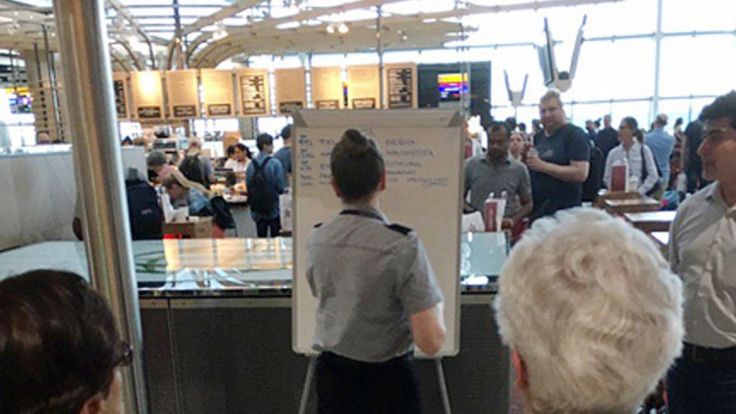 a member of British Airways staff writing gate information on a white board at Heathrow Airport