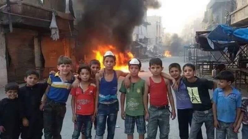 Un grupo de niños en Alepo junto a una pila de ruedas ardiendo.