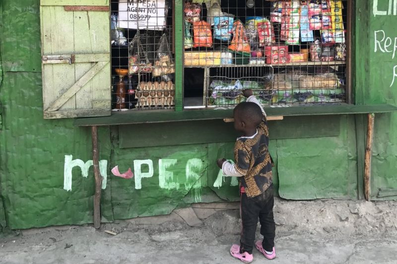 Young boy standing in front of M-Pesa agent shop