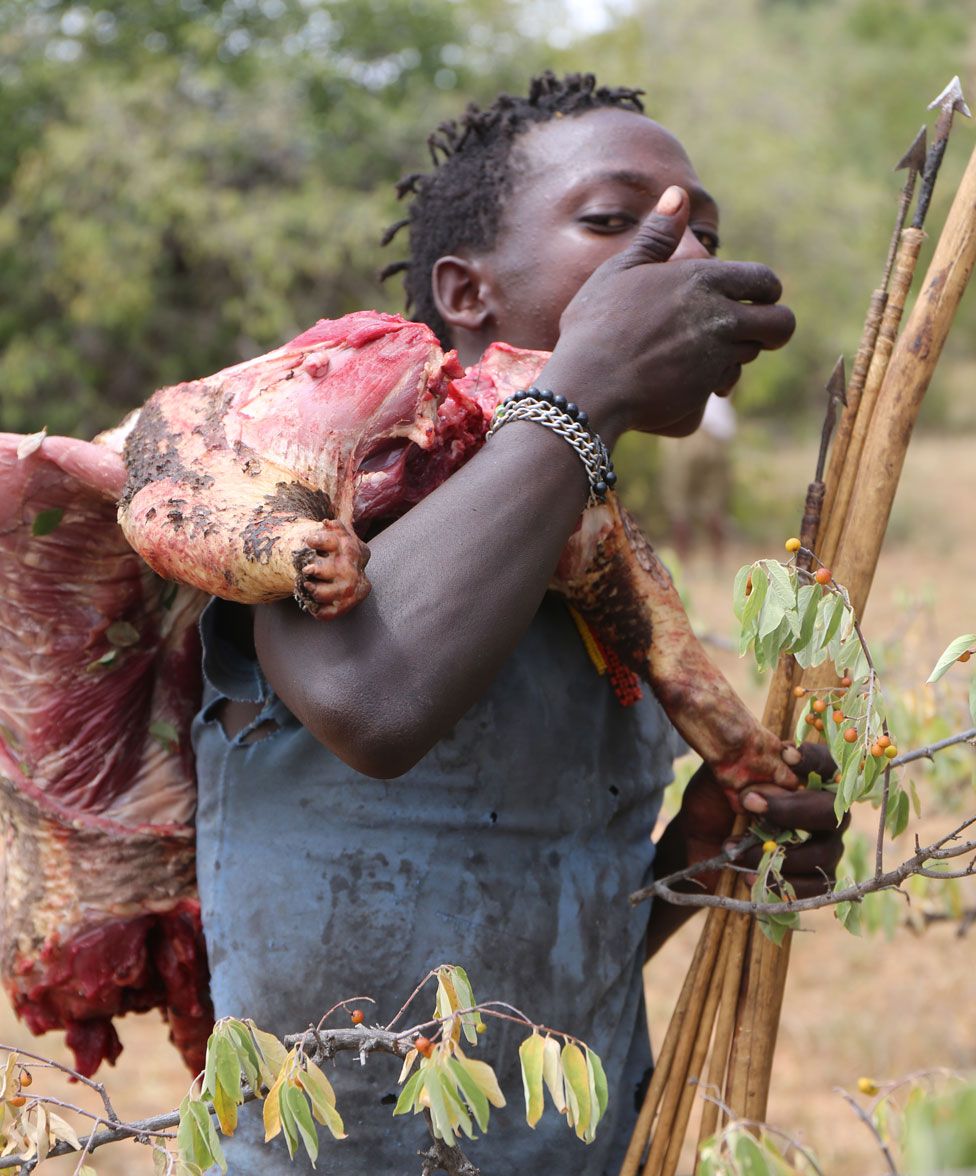 Homem hadza com arco, flecha e um pedaço de carne