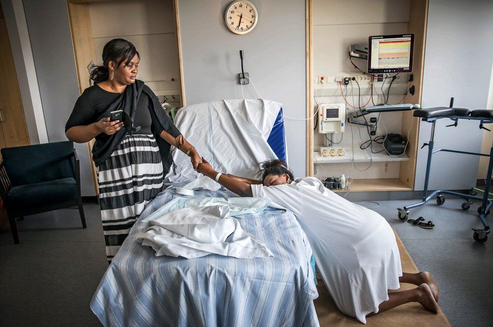 A woman holds her mother's hand as she gives birth.