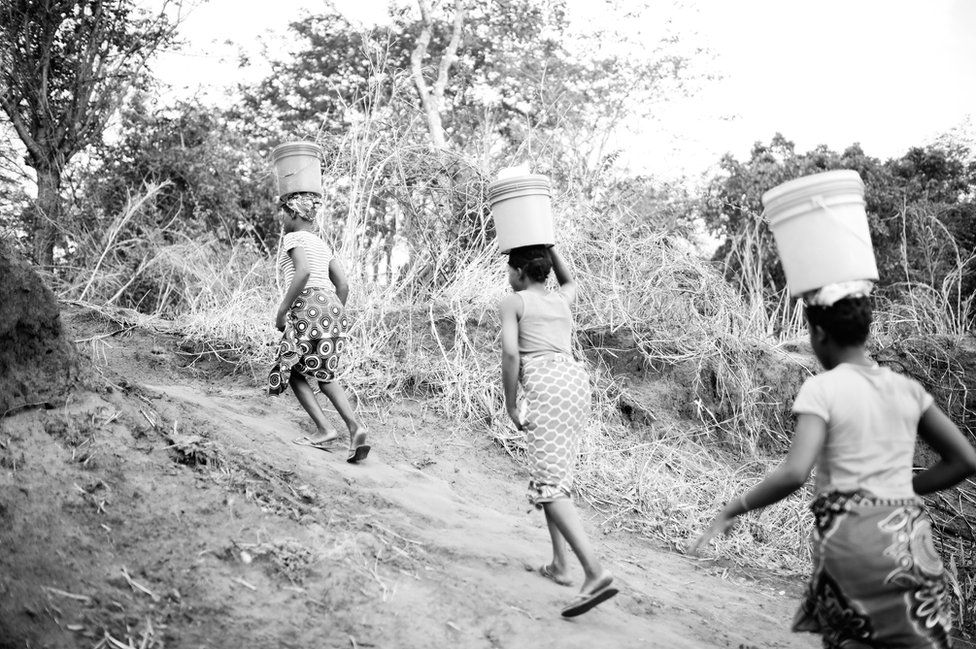 Josefina and Eudicia climb a hill with buckets balanced on their heads.