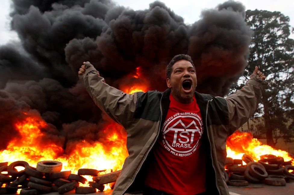 A protester spreads his arms out as he runs in front of a fire.
