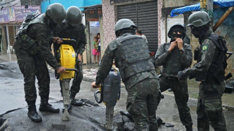 Children watch as soldiers remove a roadblock made by drug traffickers near the Vila Kennedy favela in Rio de Janeiro, on February 23, 2018.