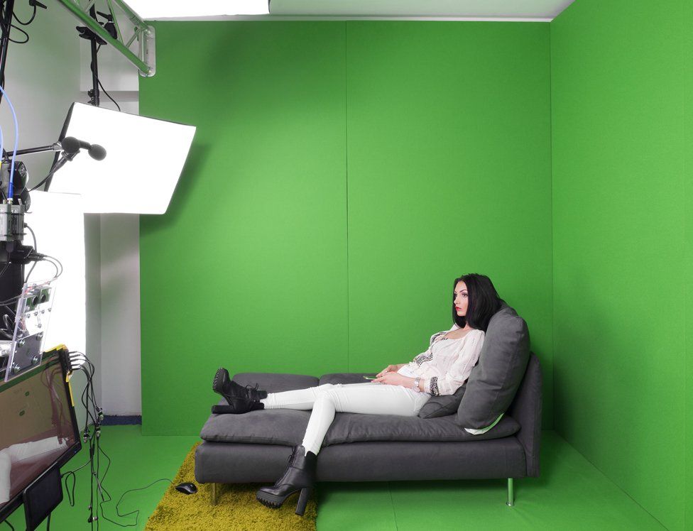 a model poses in a green-screen studio