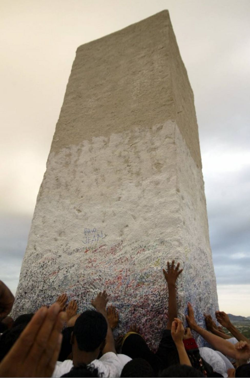 Muslim pilgrims touch a holy pillar on top of Mount Arafat, where according to Muslim tradition Prophet Mohammed delivered last sermon 14 centuries ago, as the annual hajj pilgrimage reaches its climax 19 January 2005. Nearly two million faithful from across the globe spent the night in a city of tents in a valley close to the Saudi holy city of Mecca before heading at dawn to Mount Arafat to perform the ritual symbolizing the Last Judgement, one day before Eid al-Adha, or Feast of the Sacrifice, which marks the end of the hajj. AFP PHOTO/KARIM SAHIB (Photo credit should read)