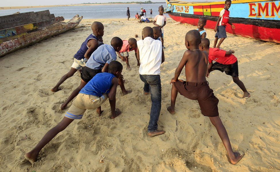 A group of young boys stretch their legs before playing a game of football on the beach