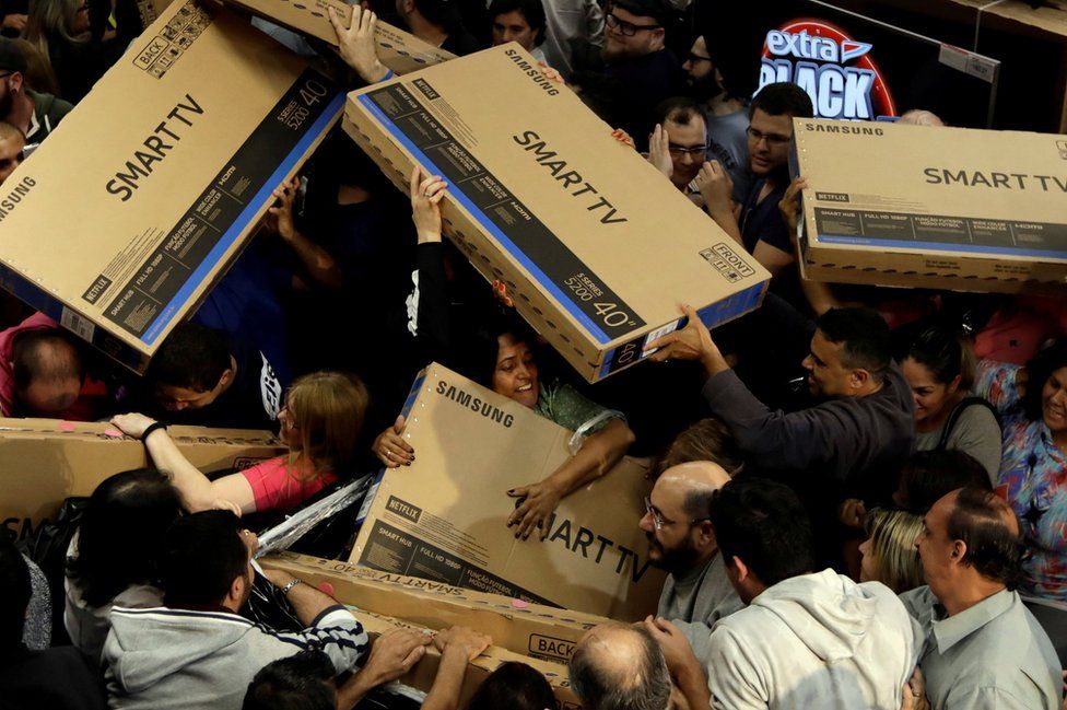 Pessoas carregando caixas de TV numa liquidação da Black Friday