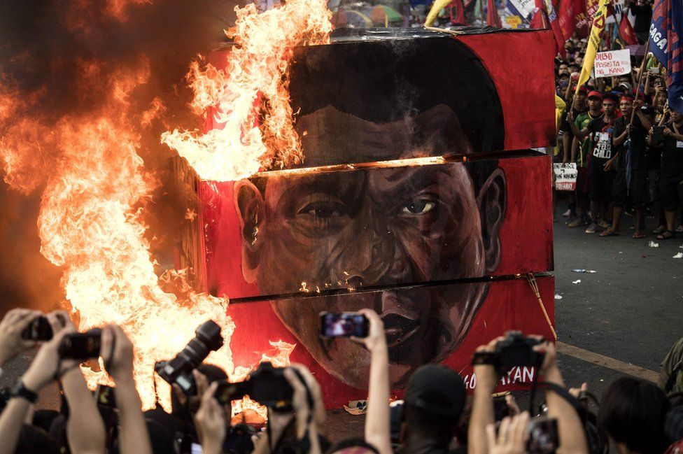 An effigy burns while people take photographs.