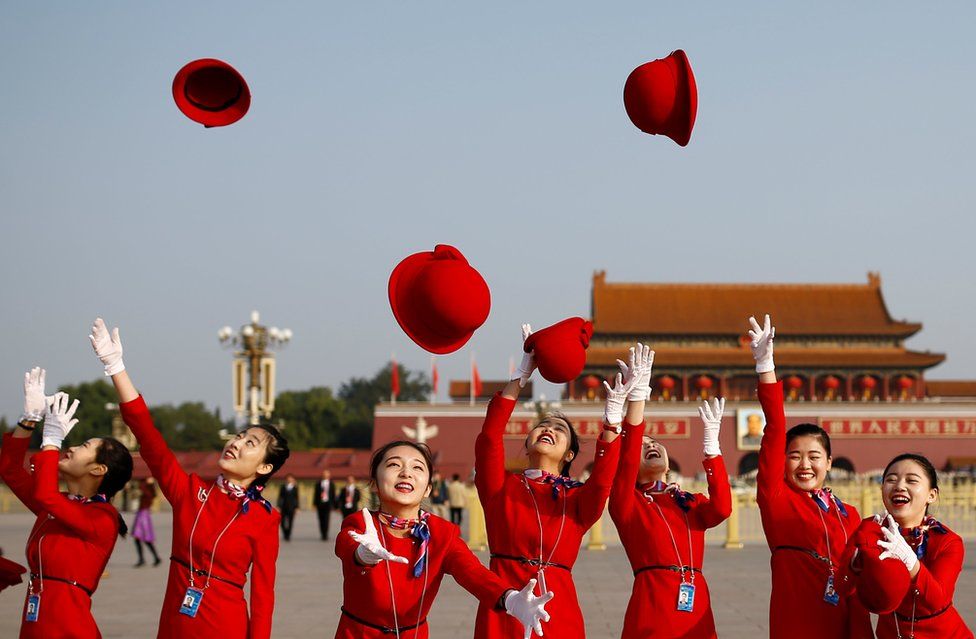 Secretarias del gobierno lanzan sus sombreros en el aire mientras posan para los fotógrafos en la Plaza Tiananmen.