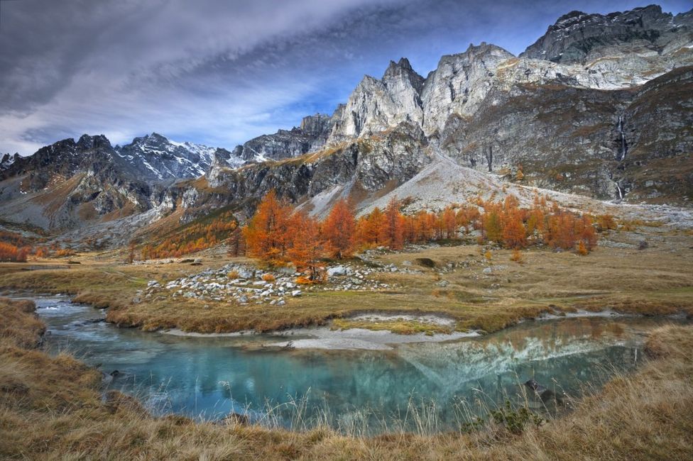 Paisaje montañoso y rocoso con un río y árboles de naranja.