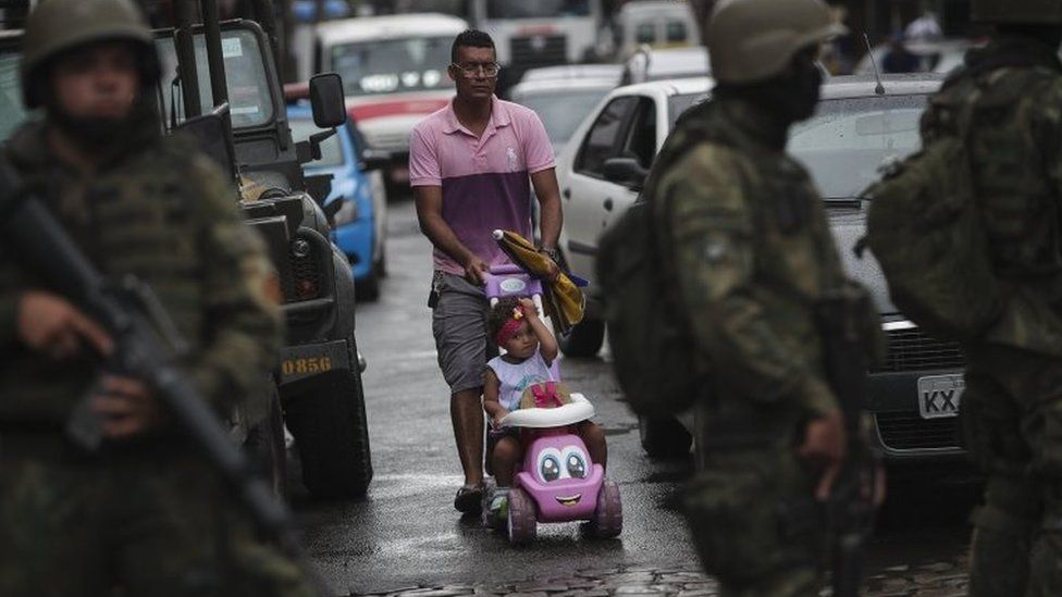 A man passes by a group of soldiers that participate in a security operation in Rio de Janeiro, Brazil, 23 February 2018