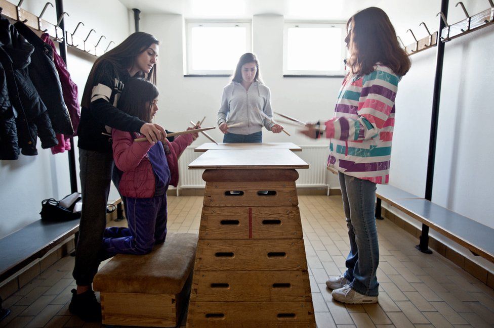 A group of girls practice drumming on wood