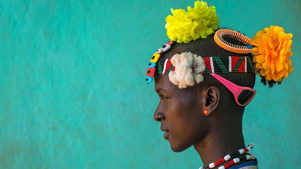 Etiyopyalı Bana kabile üyesinin başında plastik çiçek, güneş gözlüğü ve bantlardan renkli bir kompozisyon.