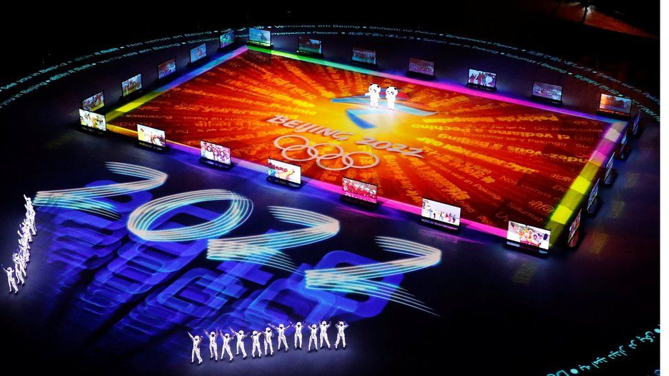 Figures gather around a giant projected logo of the Beijing 2022 Olympics