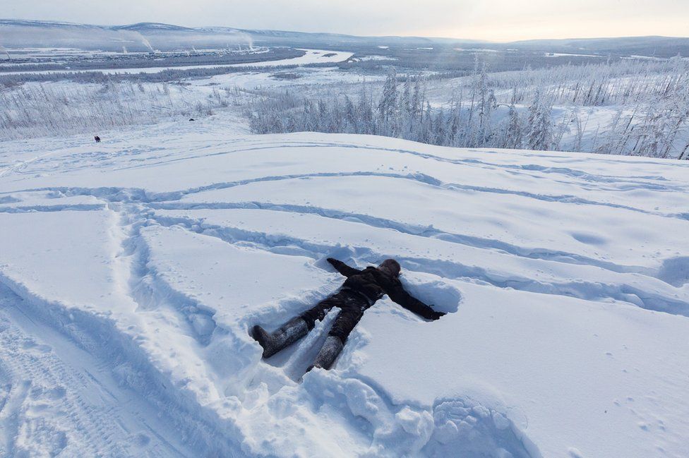 Ayal lays down in the snow on the heights of Verkhoyansk while waiting for his mother and some of her friends to come up the hill. The smoke coming out of the coal power stations of the village can be seen in the background.