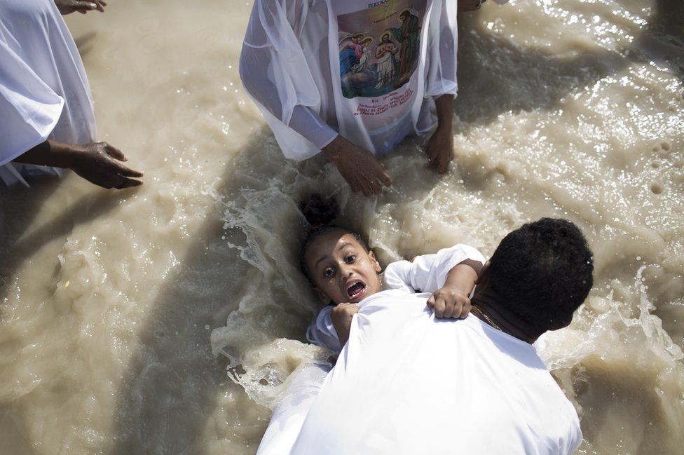 Criança de olhos arregalados ao ser batizado em Qasr al-Yahud no rio Jordão.