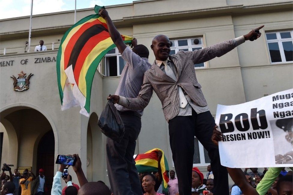 People wave national flags as they celebrate outside the parliament in Harare, after the resignation of Zimbabwe's president Robert Mugabe on November 21, 2017.