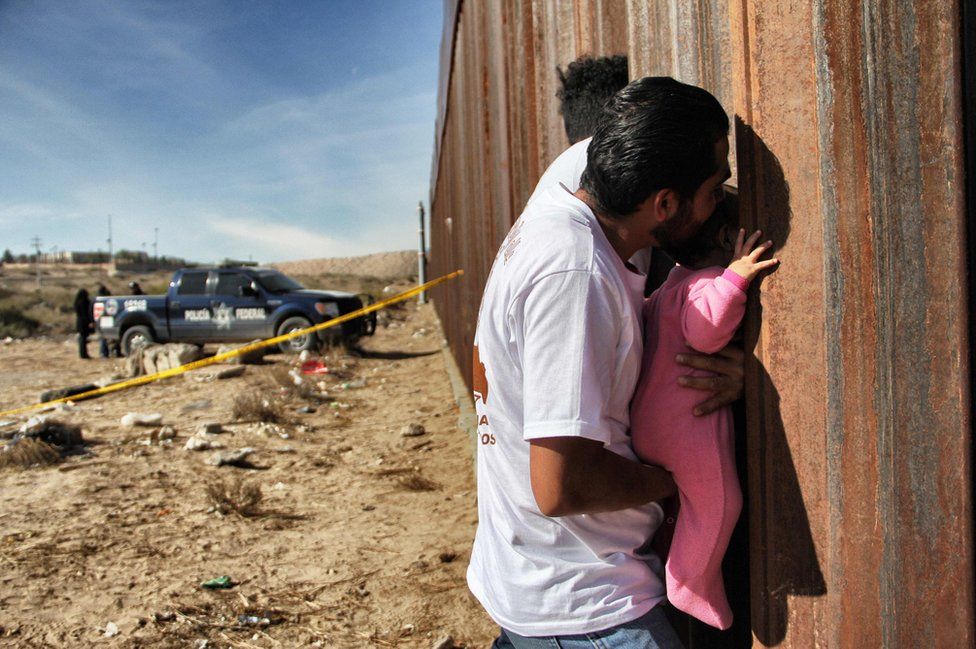 Homem segura criança no muro que separa EUA e México em 10 de Dezembro de 2017.