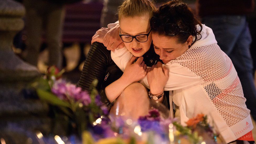 Dos mujeres se abrazan frente a los homenajes a las víctimas del atentado en Manchester.