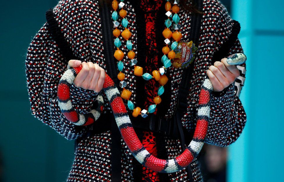 Un modelo femenino sostiene una serpiente de colores brillantes