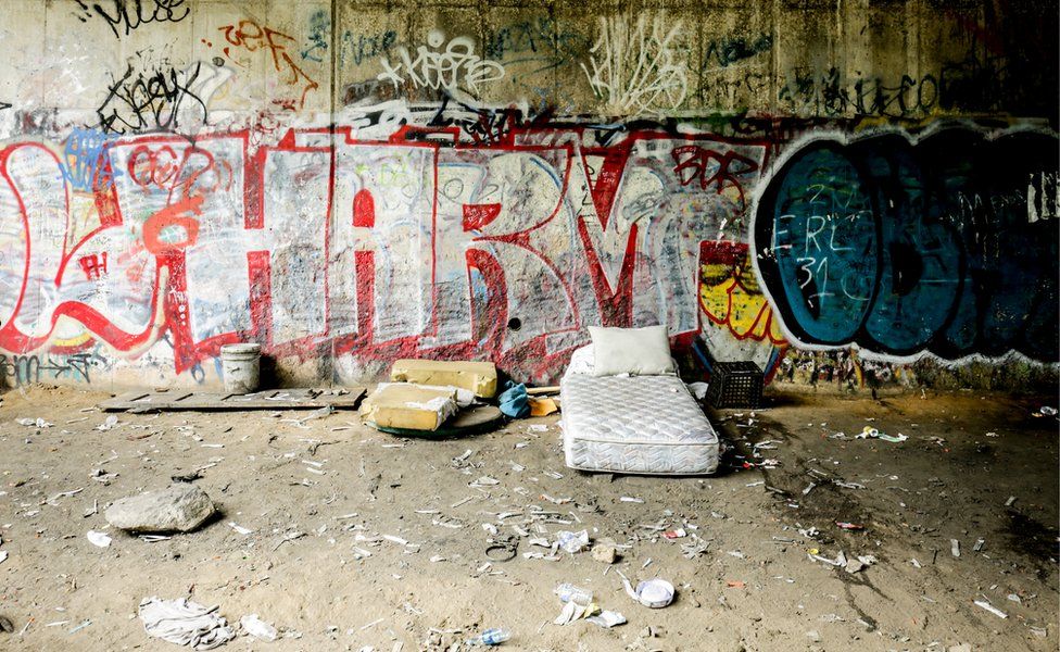 A bed sits empty on the side of the tracks, surrounded by used needles