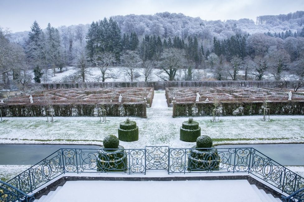 Un laberinto en un jardín cubierto de nieve con bosque de fondo.