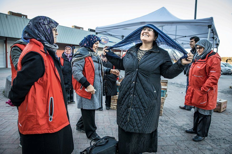 A group of women gather, with one tying on a headscarf.