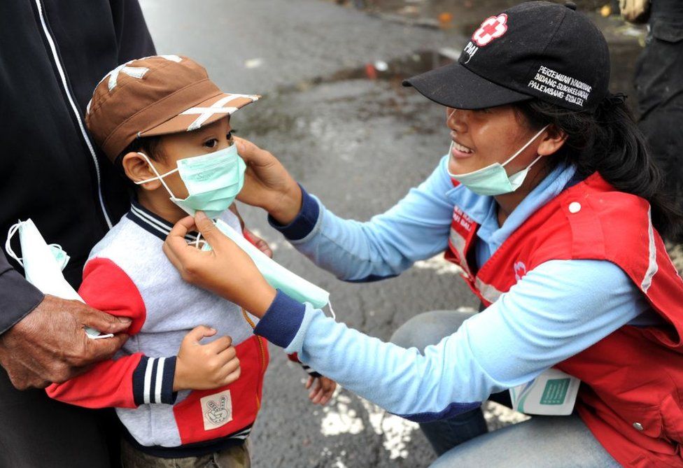 Una voluntaria le pone una mascarilla a un niño.