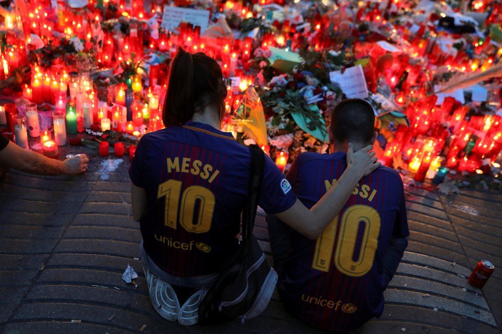 Two people sit in front of a memorial.
