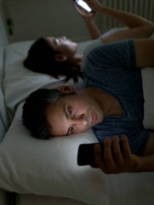 Una pareja en la cama con celulares