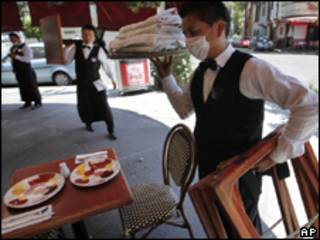 Garçom usando máscara contra a gripe recolhe pratos de restaurante fechado na Cidade do México (AP, 28/4)