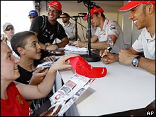 Lewis Hamilton e Jenson Button (de fundo) assinando autógrafos