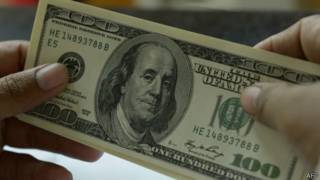 Una persona sostiene un billete de cien dólares estadounidenses